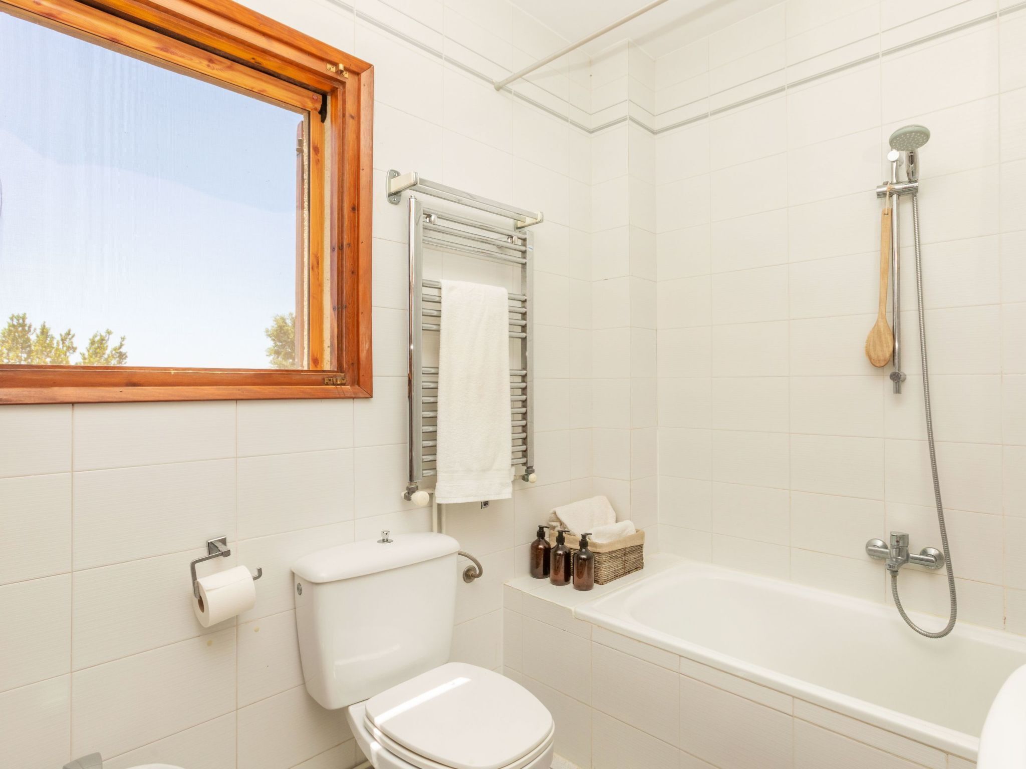 A bathroom with a toilet, a bathtub, a window, and a towel rack.