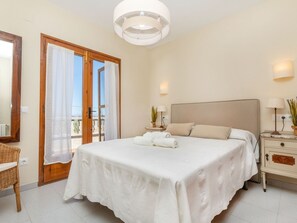 A bedroom with a bed, a nightstand, a lamp, a potted plant, and a view through a door.