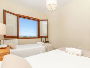 Une chambre d’hôtel avec deux lits, une fenêtre avec des stores, une table de chevet et une lampe.