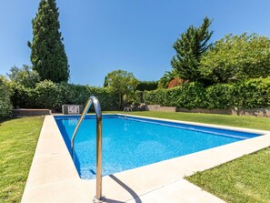 Une piscine rectangulaire avec un escalier en métal, entourée d’une pelouse bien entretenue et de divers arbres.