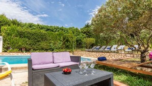 A poolside area with a wicker sofa, a table with wine glasses and fruit, and lounge chairs. - Vacation home Antem by Interhome (Lloret de Mar)