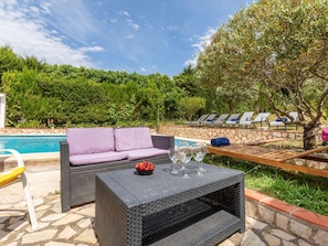 A poolside area with a wicker sofa, a table with wine glasses and fruit, and lounge chairs. - Vacation home Antem by Interhome (Lloret de Mar)