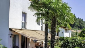 Une maison à deux étages dotée d’un patio couvert, d’un jardin avec différentes espèces de plantes et d’un palmier.