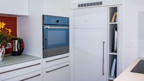 Une cuisine moderne avec des meubles blancs, un four bleu et une bibliothèque intégrée.