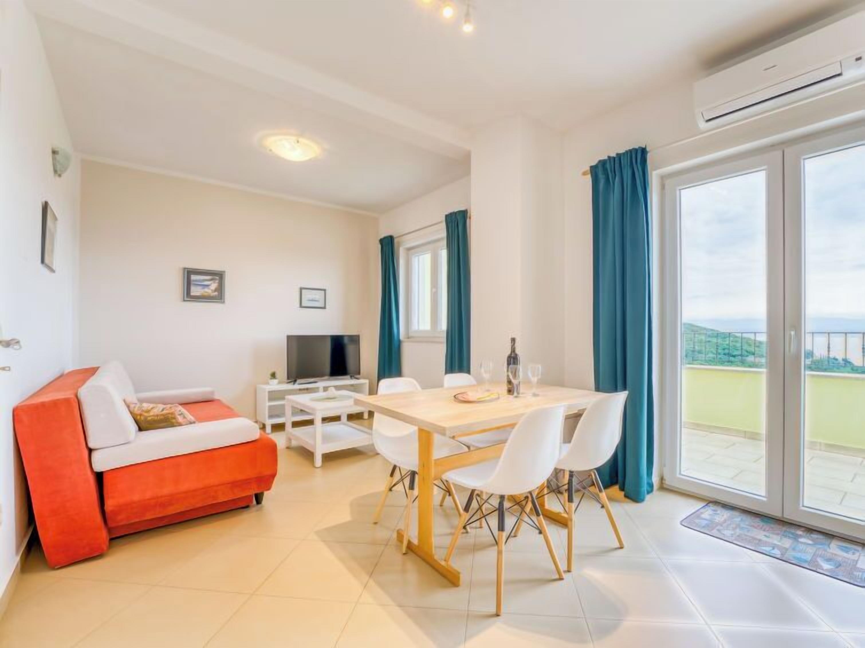 Un salon moderne comprenant un canapé, une table à manger avec des chaises, un téléviseur et un balcon avec des rideaux.