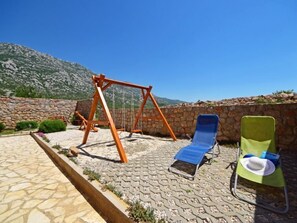 A patio with a swing set, two lounge chairs, and a stone wall with a mountain view.