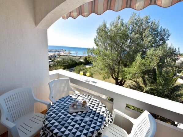 Een balkon met een tafel en stoelen, met uitzicht op een strand en bomen.