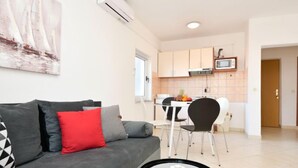 Een moderne woonkamer met een grijze bank, een kleine ronde tafel en een keuken met witte kasten en een magnetron.