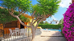 Un patio con sendero de piedra, un árbol, una piscina y un edificio blanco con tejado de tejas.