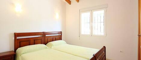 A bedroom with a wooden bed frame, two bedside tables, a window with bars, and a door.