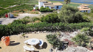 Propiedad costera con un edificio blanco, un patio con mesa y sillas, y vistas al mar y campos.
