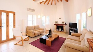 Un salón espacioso con techo alto, vigas de madera, chimenea, televisor y sofá.
