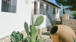 Un edificio blanco con techo de tejas, una escalera y una planta de cactus en primer plano.