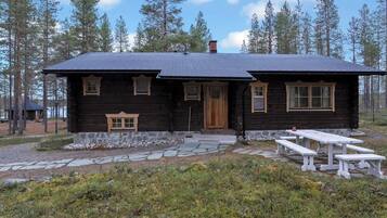 A wooden cabin with a stone pathway leading to the entrance, surrounded by a forest.