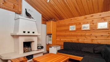 A cozy cabin interior with a fireplace, wooden walls, a sofa, and a table.