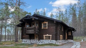 A log cabin with a stone foundation, a balcony, and a gravel driveway.