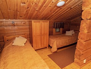 Quarto de cabana de madeira com duas camas, um guarda-roupa e uma janela com cortinas.