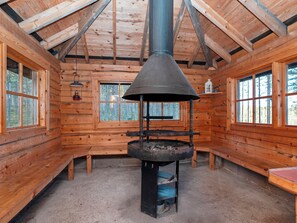 L’intérieur d’une cabane en rondins, avec un poêle à bois central, des murs en bois et de grandes fenêtres.