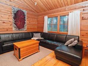 A log cabin interior with a black leather sofa, a wooden coffee table, and a large window with curtains. - Vacation home Siula by Interhome (Kuusamo)