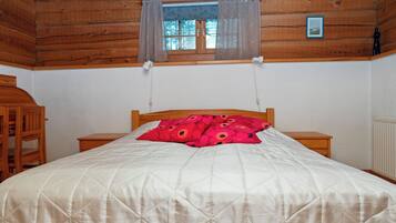 A wooden cabin bedroom with a bed, a nightstand, a chair, a window with curtains, and a picture on the wall.