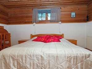 A wooden cabin bedroom with a bed, a nightstand, a chair, a window with curtains, and a picture on the wall. - Vacation home Siula by Interhome (Kuusamo)