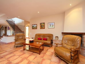 Un salón amplio con chimenea, sofás de cuero, una mesa de centro y una escalera.