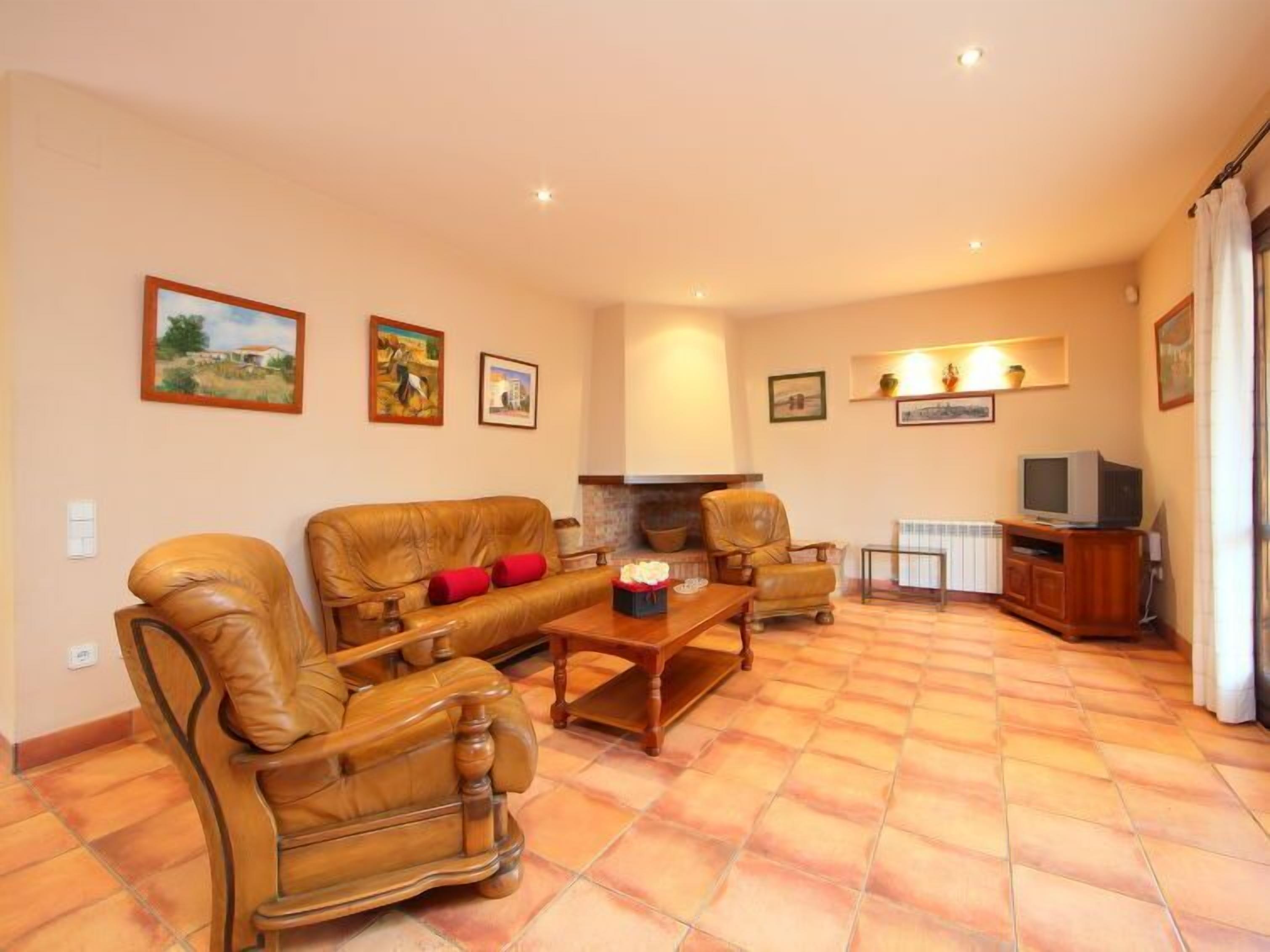 A living room with a sofa, armchairs, a coffee table, and a fireplace. There are framed pictures on the walls and a television on a wooden stand.