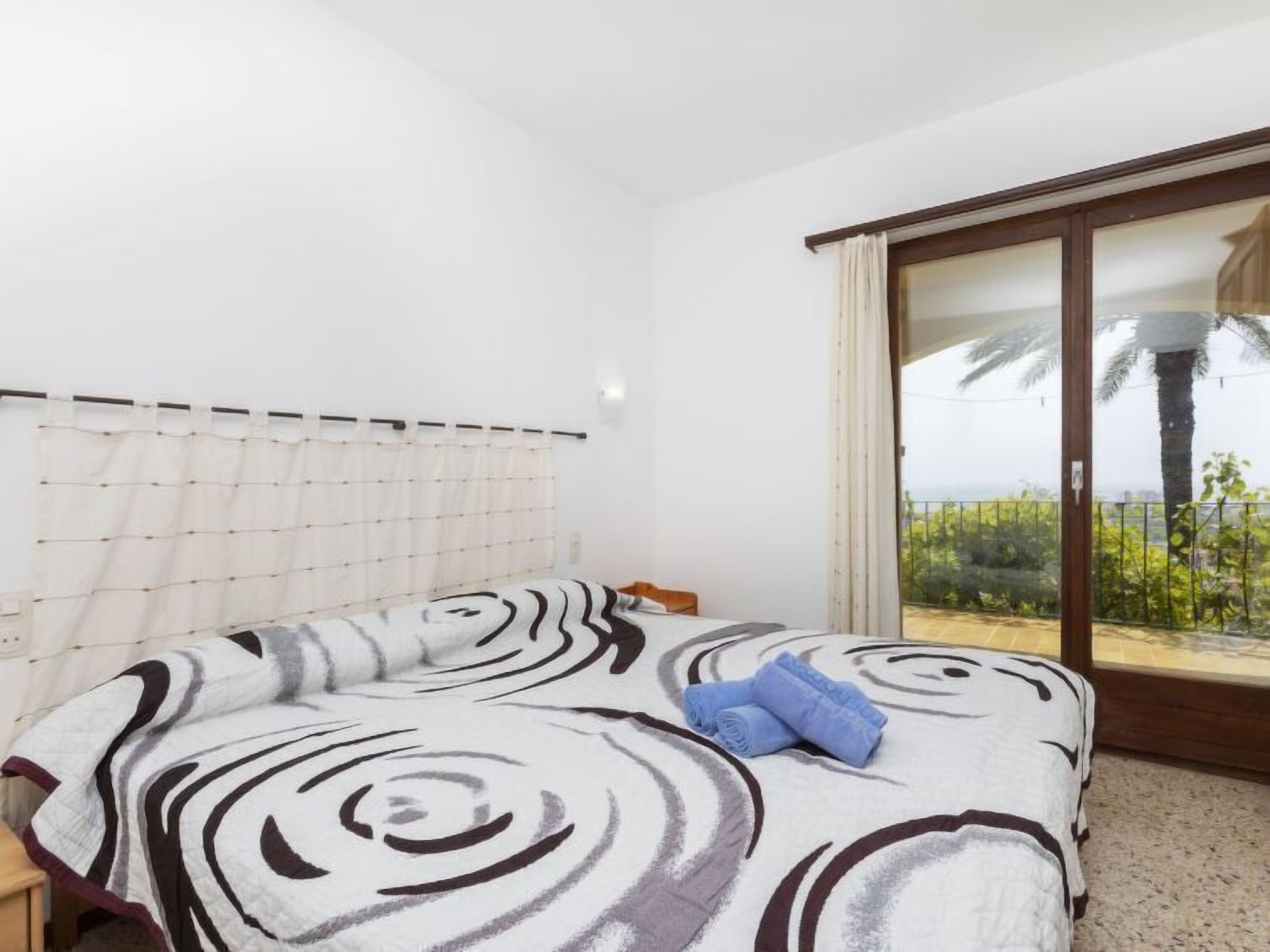 Een slaapkamer met een bed, een raam met gordijnen en uitzicht op groen.