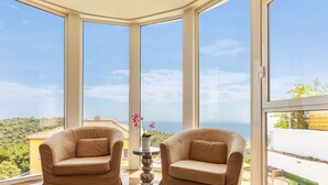 A room with two leather armchairs, a small table with a vase, and large windows offering a view of the sea and greenery. - Vacation home Gaudí by Interhome (Lloret de Mar)