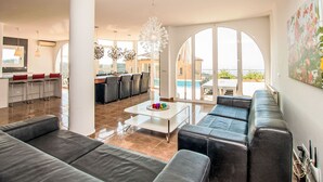A modern living room with a sofa, a coffee table, and a dining area with chairs. There is a large window with a view of the outdoors. - Vacation home Gaudí by Interhome (Lloret de Mar)