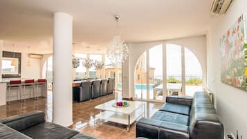 Un salon moderne comprenant un canapé, une table basse et un coin repas avec des chaises. Une grande fenêtre offre une vue sur l’extérieur.