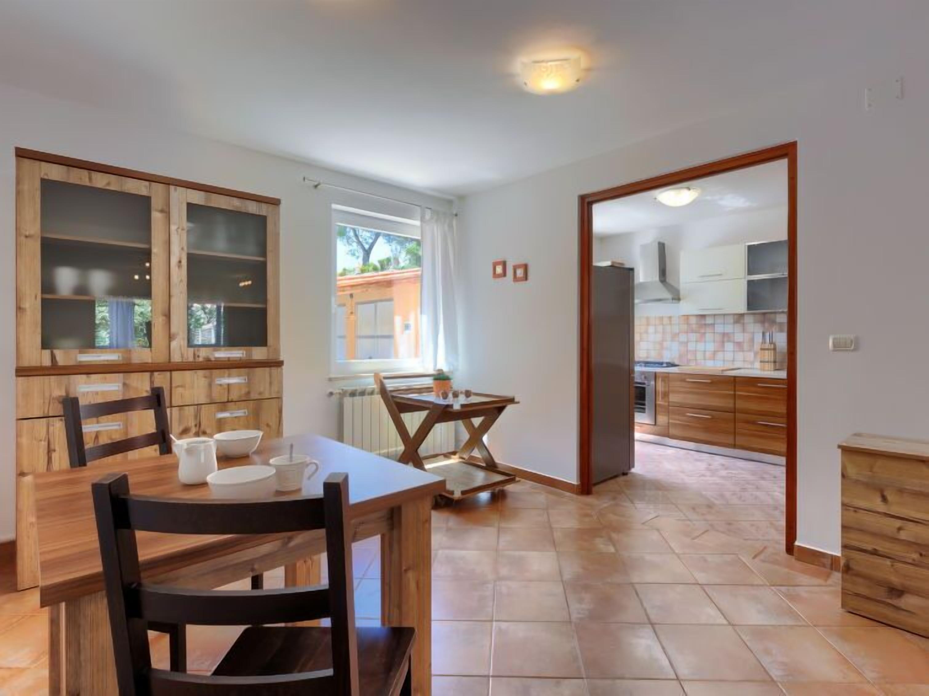 A dining area with a wooden table and chairs, a window with curtains, and a view of the outside.
