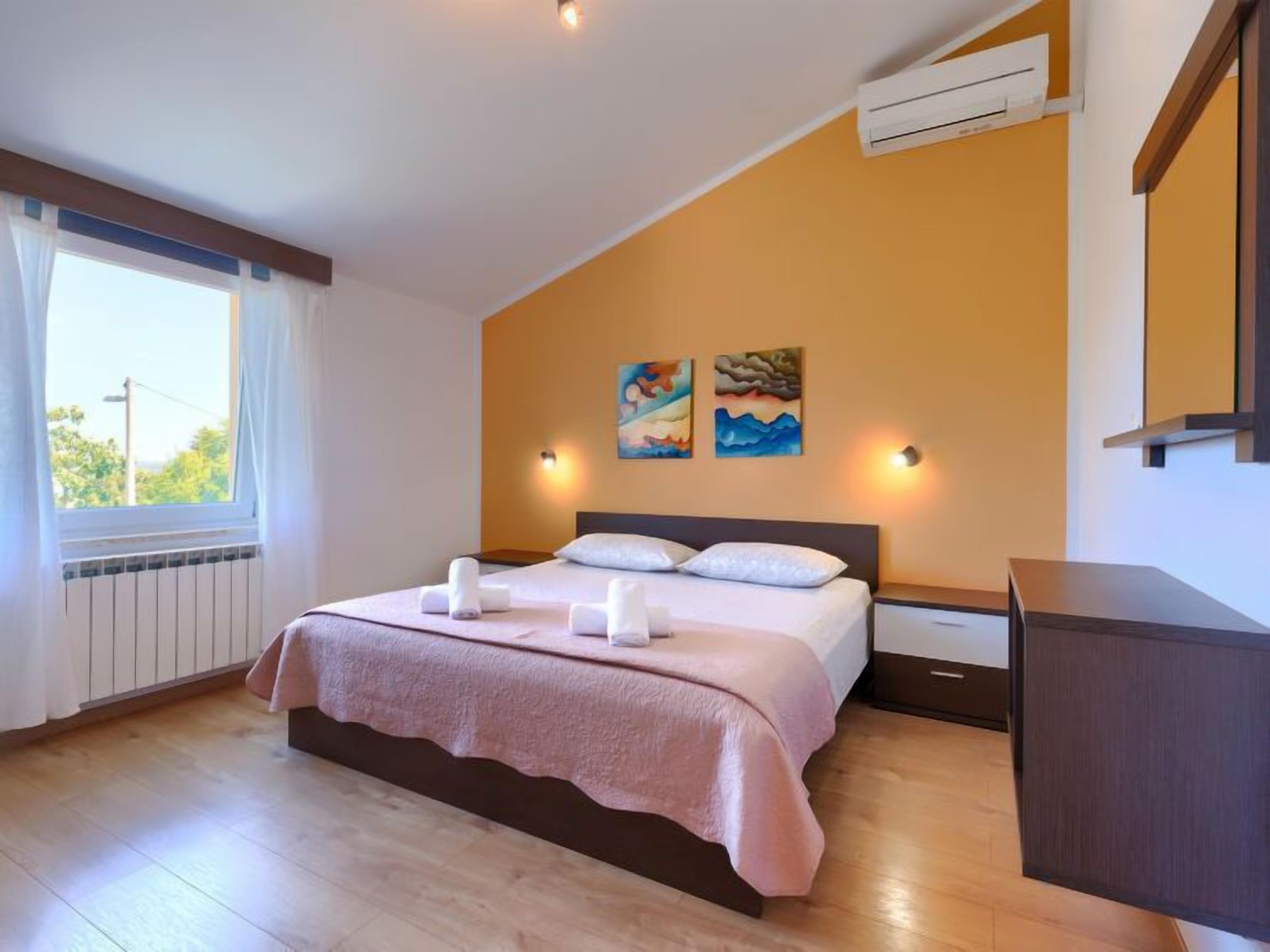 A bedroom with a bed, two wall-mounted lights, a radiator, and two paintings.