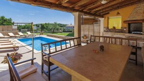 A poolside area with a bar, seating, and a stone fireplace. - Licardo by Interhome (Štinjan)
