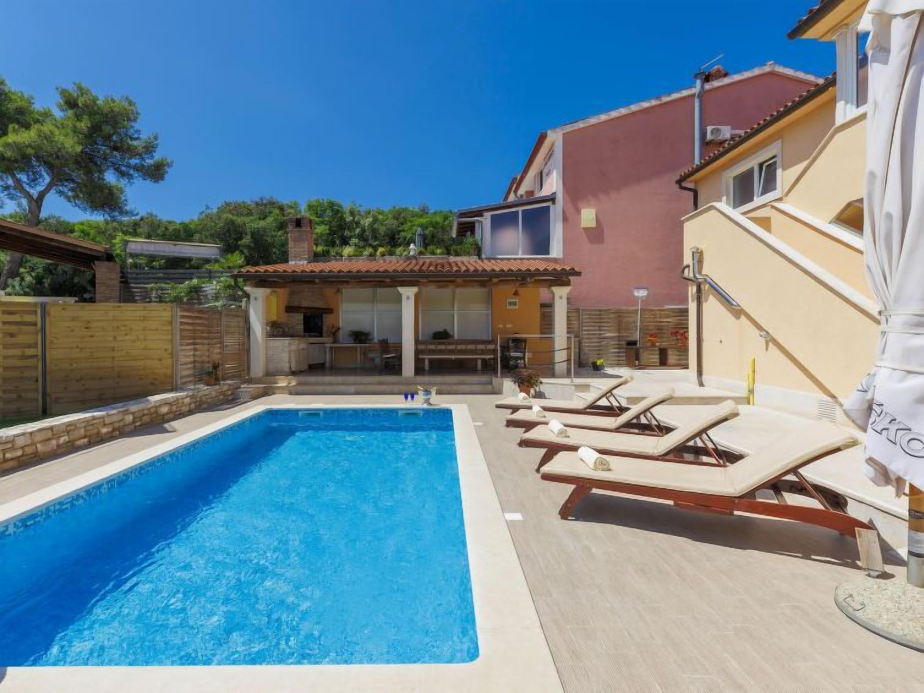 Una piscina amb gandules, un porxo cobert i un edifici amb teulada enrajolada.