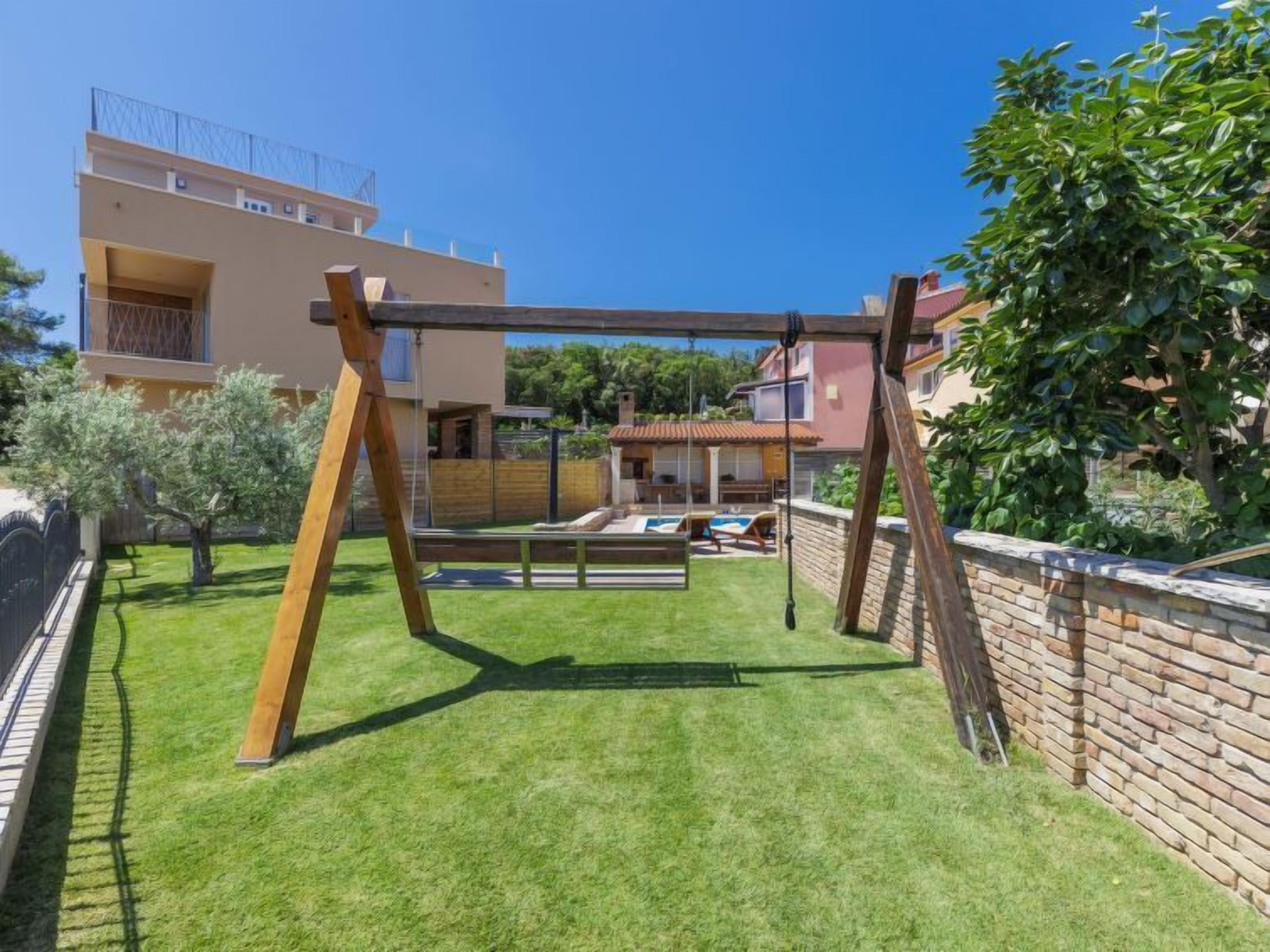 A backyard with a wooden swing set, a pool, and a brick wall.