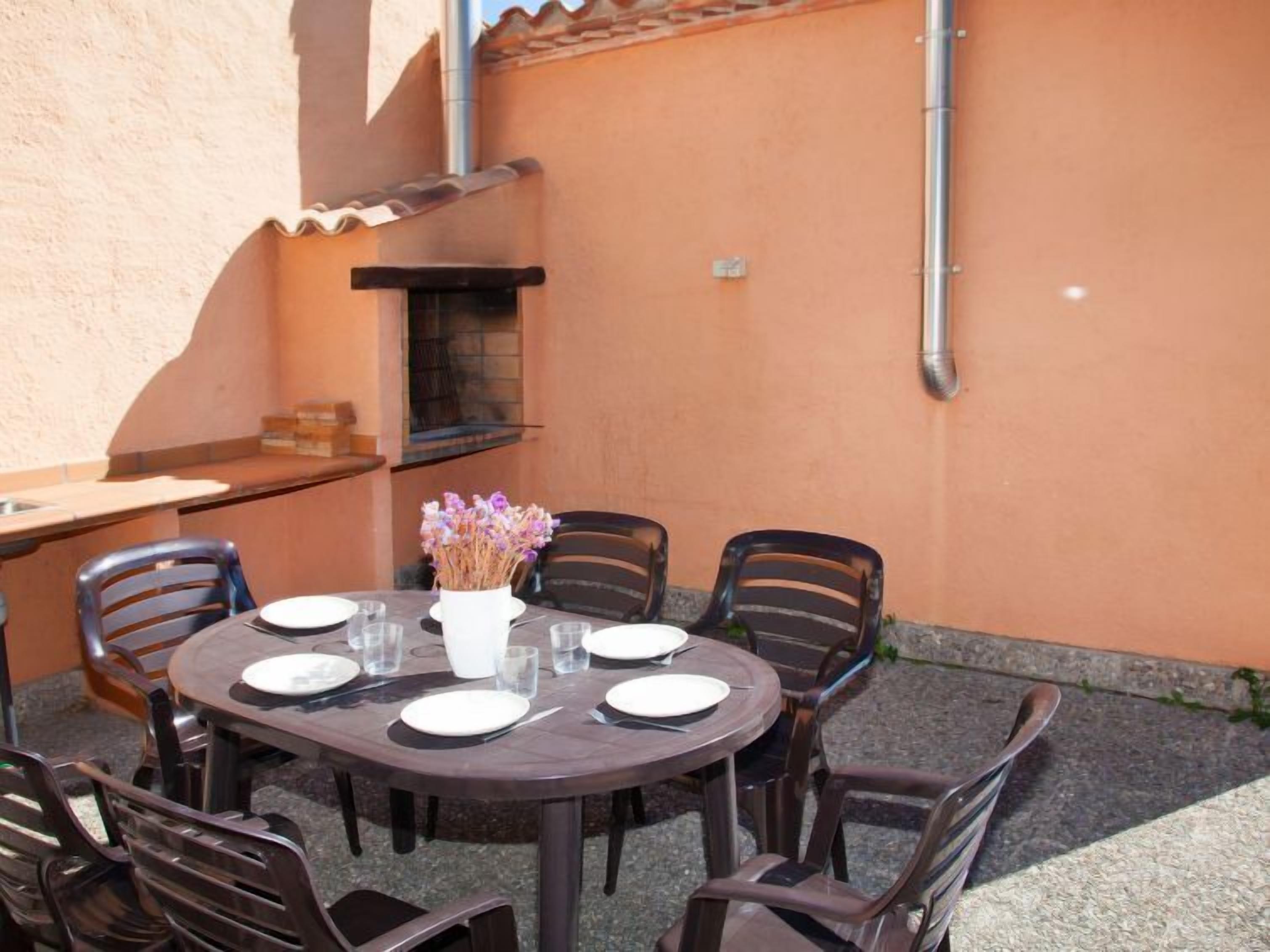 An outdoor dining area with a round table, six chairs, and a vase of flowers.