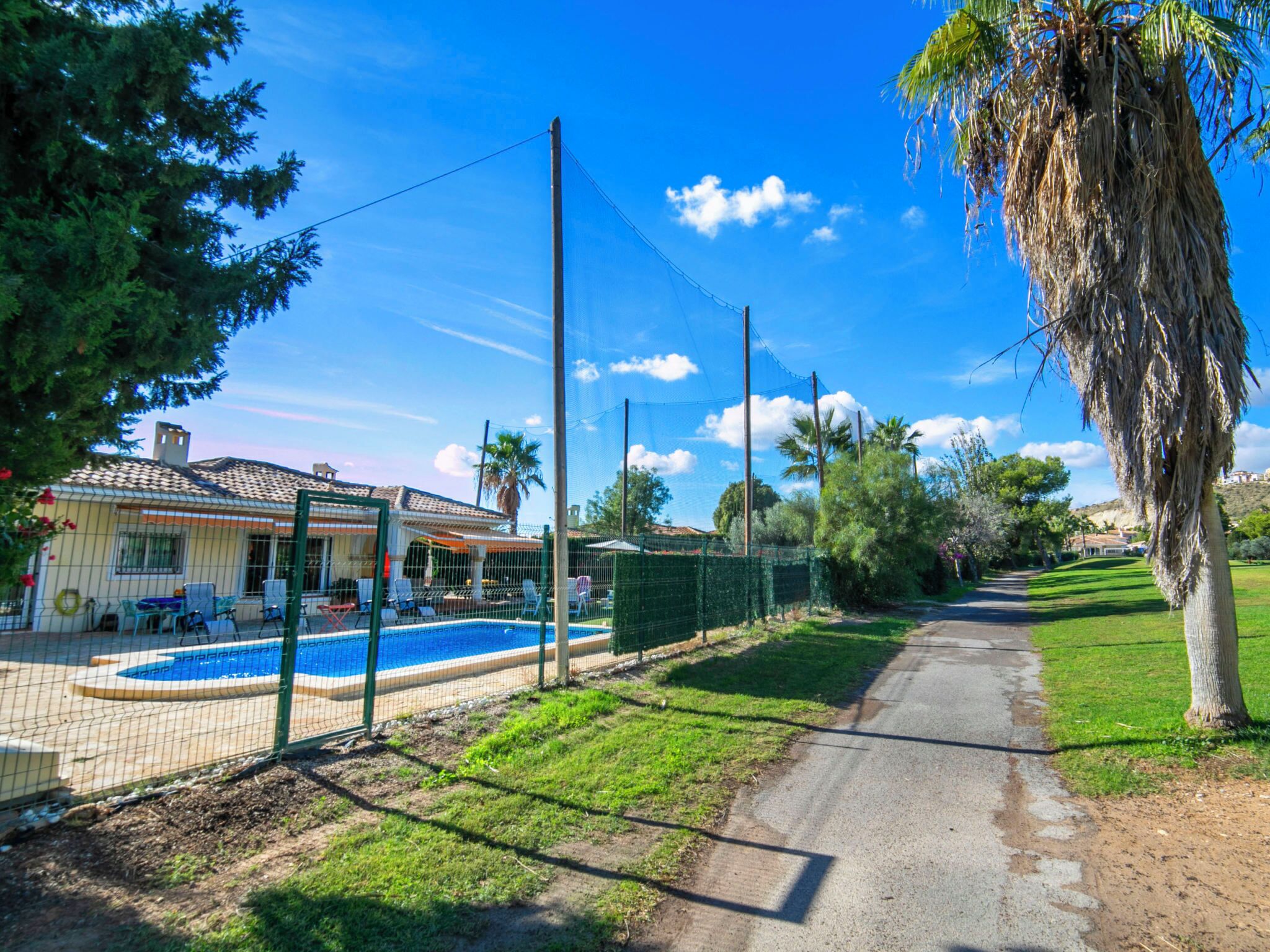 Il s’agit d’une propriété résidentielle dotée d’une piscine, d’une terrasse clôturée et d’un chemin menant à une zone vallonnée, parsemée d’arbres, d’où l’on peut apercevoir une maison au loin.
