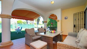 A covered outdoor seating area with wicker furniture, a table with a bottle and glasses, and a clock on the wall. - Bonalba Golf, Urb. Los Naranjos by Interhome (San Juan / Muchamiel)
