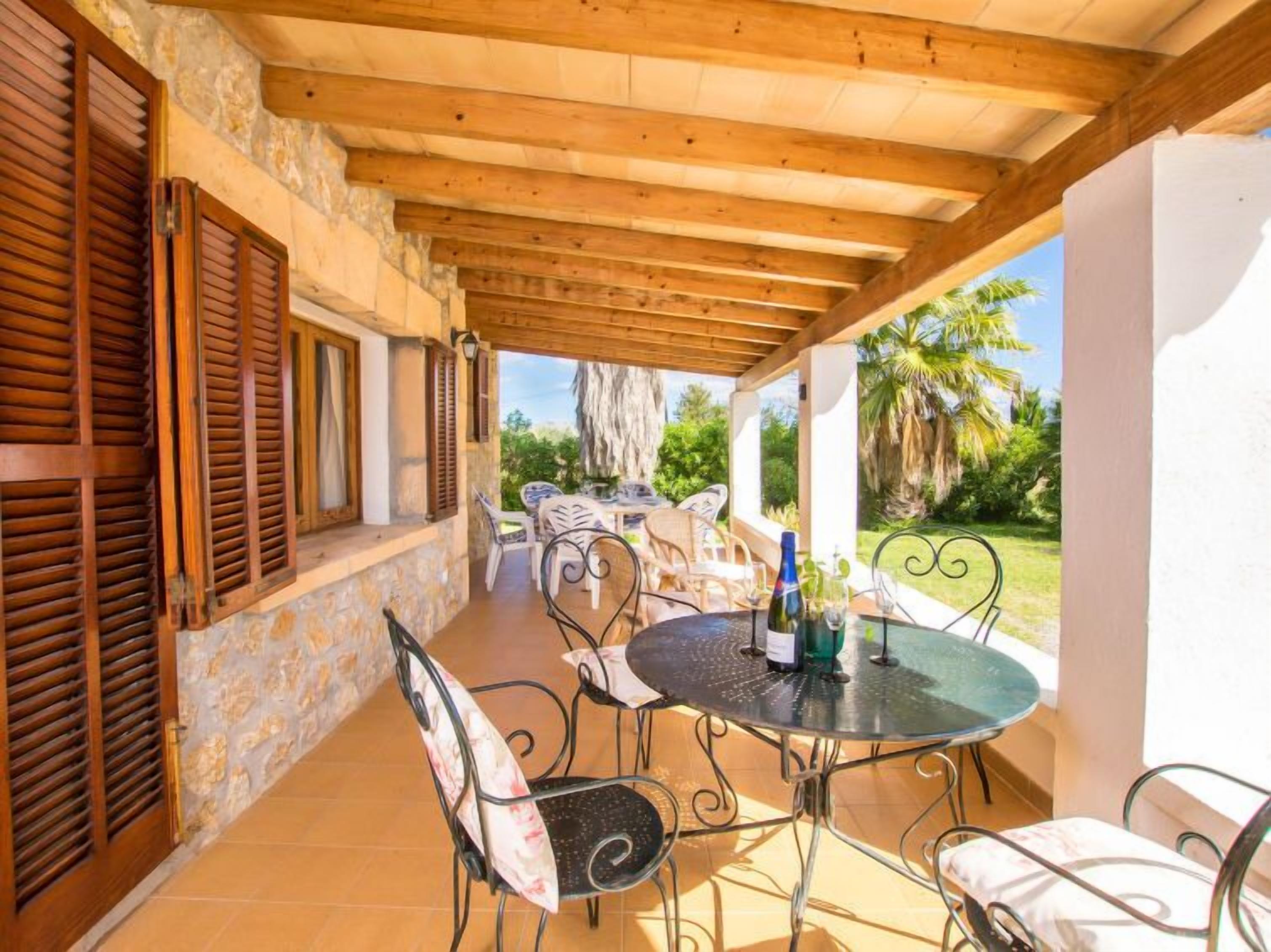 Eine überdachte Terrasse im Freien mit Steinmauern, Holzläden und Metallstühlen.