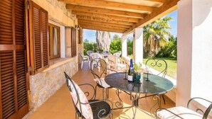 A covered outdoor patio with stone walls, wooden shutters, and metal chairs. - Can Mateu by Interhome (Pollença)