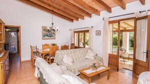 A cozy living room with a sofa, a dining table, and chairs. There is a wooden ceiling and a painting on the wall. - Can Mateu by Interhome (Pollença)