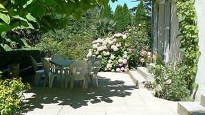 Eine Garten-Terrasse mit Tisch und Stühlen, umgeben von üppiger Bepflanzung und blühenden Pflanzen.