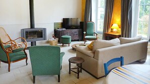 Ein gemütliches Wohnzimmer mit einer Couch, Sesseln, einem kleinen Tisch, einem Fernseher und einem Kamin.