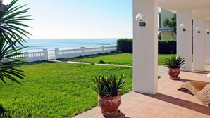 A covered outdoor area with a view of the sea, green lawn, and potted plants. - Urb.Maricel by Interhome (Alcanar)