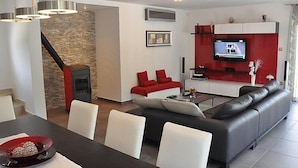 A modern living room with a fireplace, a sofa, a dining table, and a TV mounted on a red wall. - Vacation home Nicole by Interhome (Opatija/Pobri)