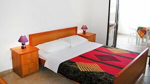 Een net opgemaakt bed met een beddengoed met een patroon, twee bedlampjes, een houten nachtkastje en een klein lade.