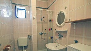 Een badkamer met toilet, wastafel, douche en een klein raam.