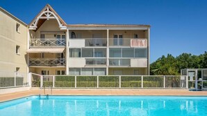 Ein zweigeschossiges Gebäude mit Balkonen, einem Swimmingpool und einem eingezäunten Bereich.