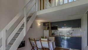 Eine moderne Küche mit dunklen Schränken, einer Mikrowelle und einem Spülbecken. Es gibt einen Essbereich mit Tisch und Stühlen sowie eine Treppe, die zu einer oberen Ebene führt.